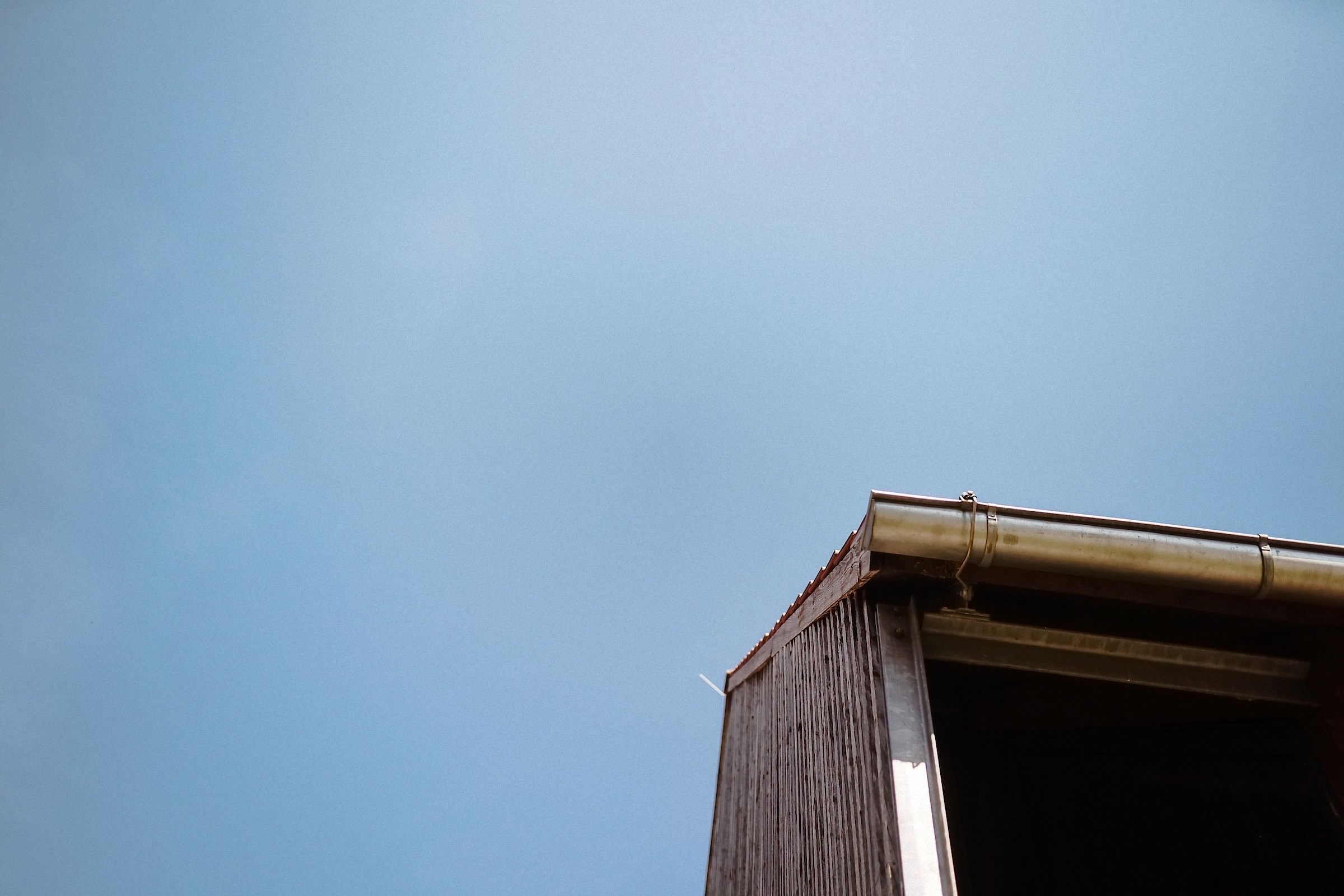 Die Dachkante eines Hauses mit Regenrinne hebt sich scharf gegen den strahlend blauen Himmel ab.