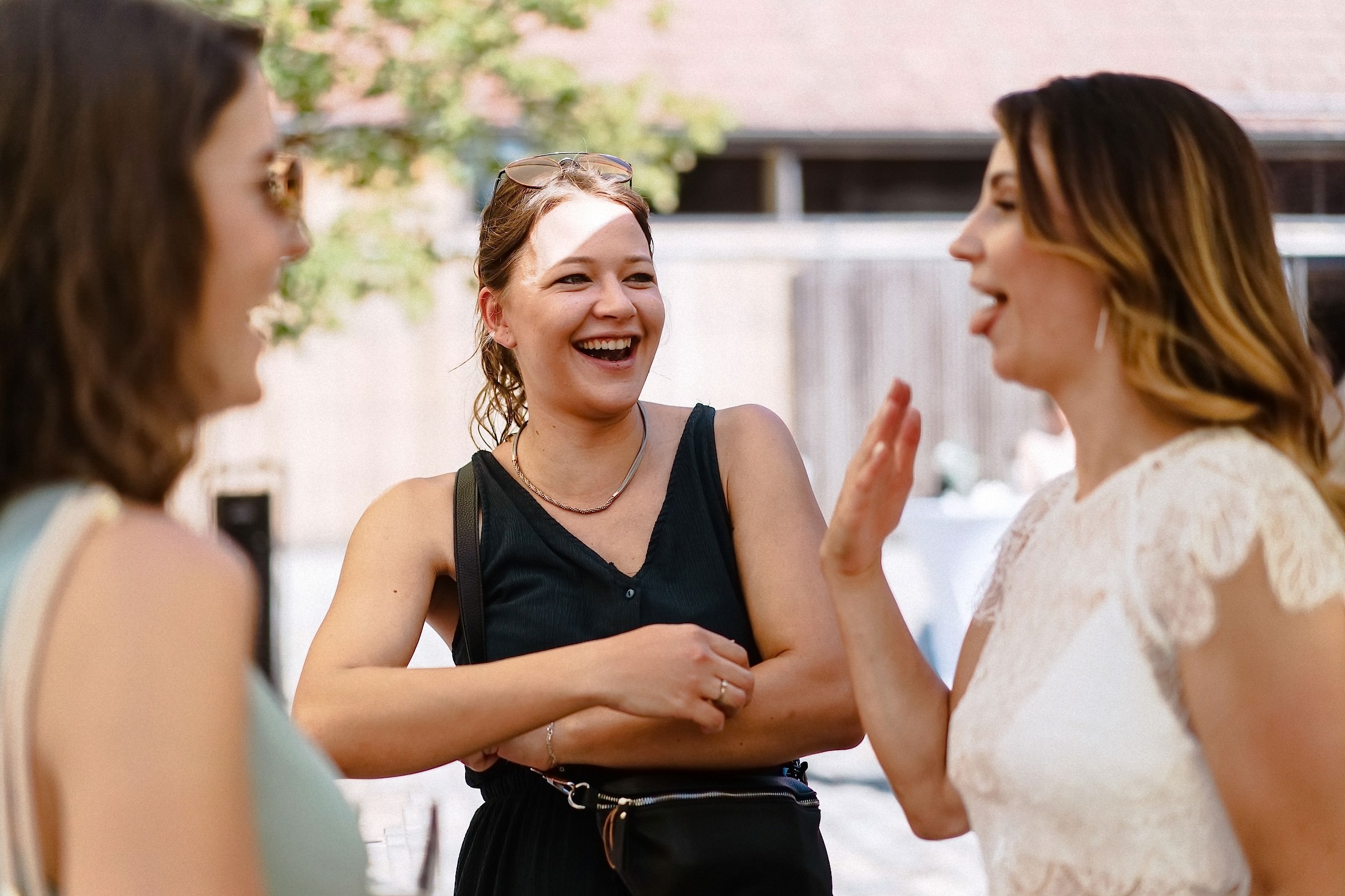 Drei Freundinnen unterhalten sich lachend im Kreis, während die Braut in weißem Spitzenkleid erzählend gestikuliert.