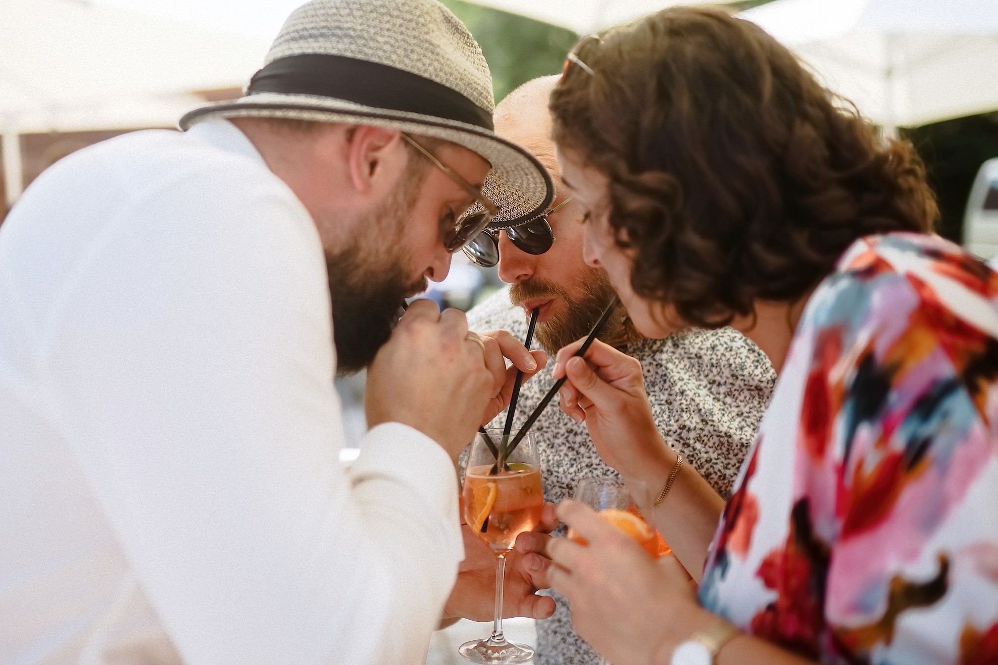 Drei Gäste beugen sich zusammen und trinken mit Strohhalmen aus einem gemeinsamen Aperol-Spritz-Glas.