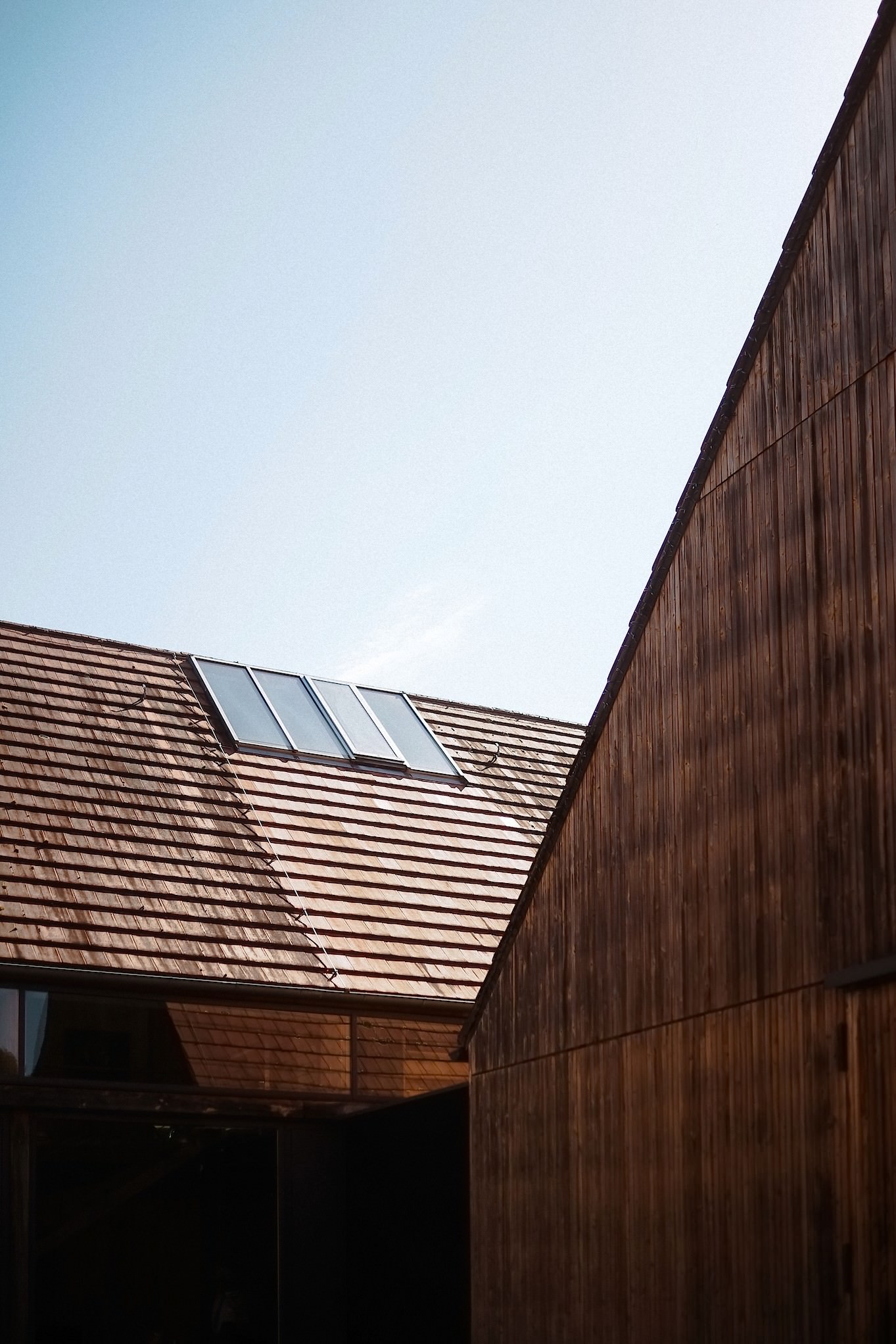 Architektonische Detailaufnahme der dunklen Holzfassade und des Ziegeldachs der Location vor blauem Himmel.