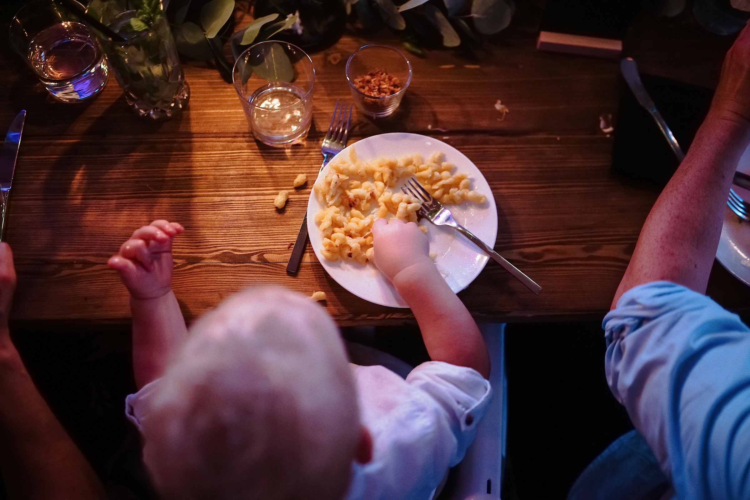 Ein Kleinkind greift von oben fotografiert mit den Fingern nach Käsespätzle auf seinem Teller.