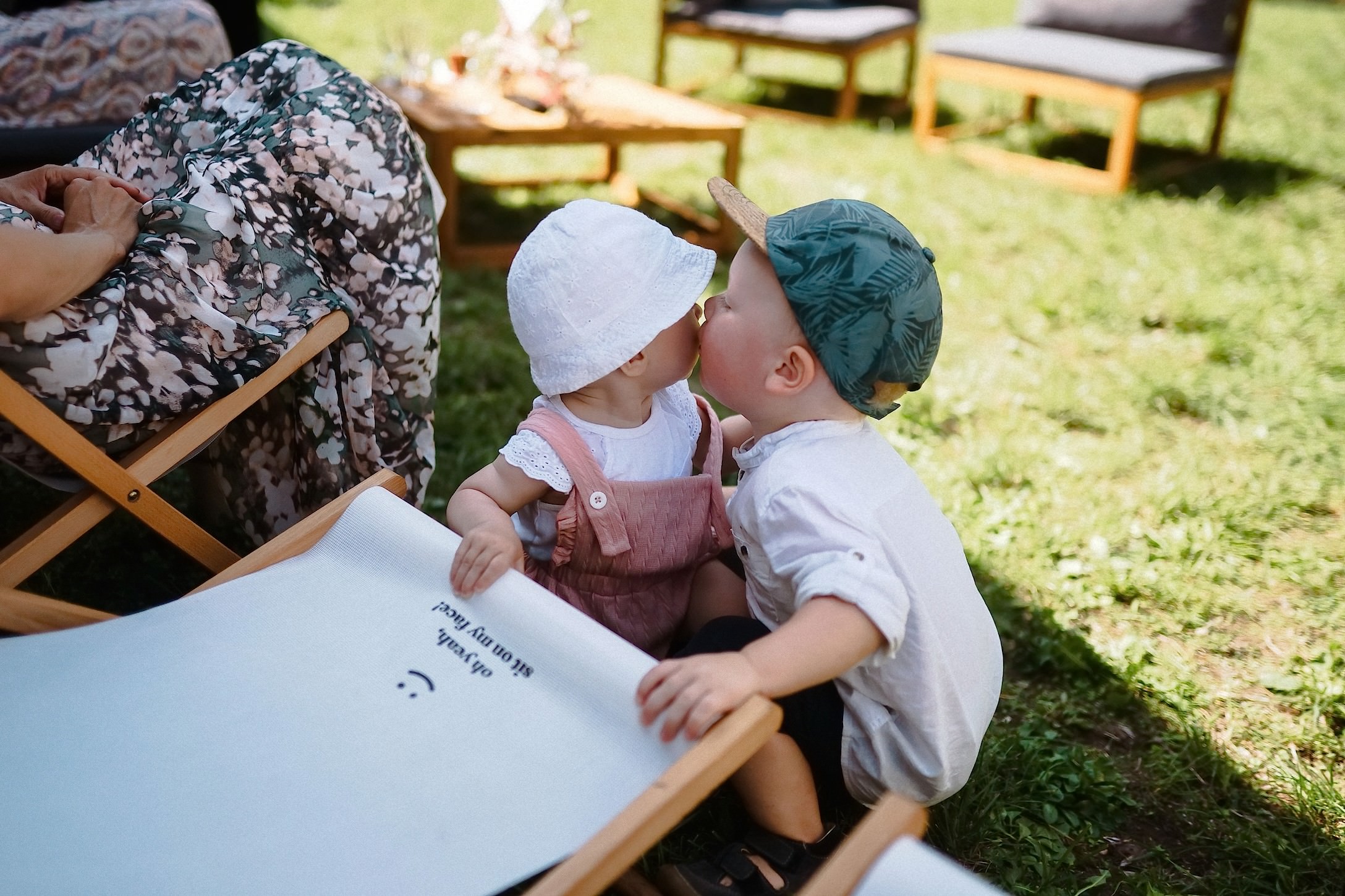 Zwei kleine Kinder mit Sonnenhüten geben sich einen niedlichen Kuss auf einer Liege im Garten.