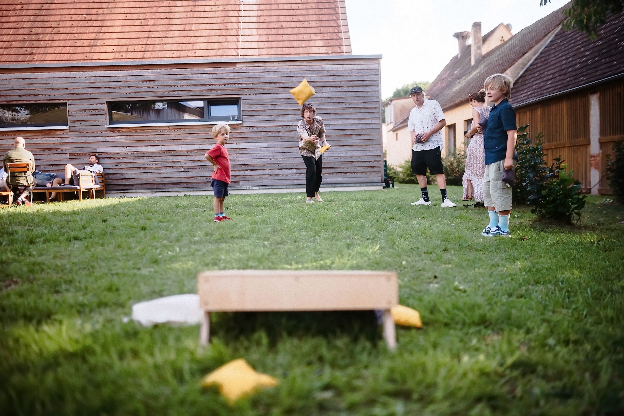 Kinder und Erwachsene spielen im Garten Kubb bei der Hochzeitsfeier vor einem Holzhaus.