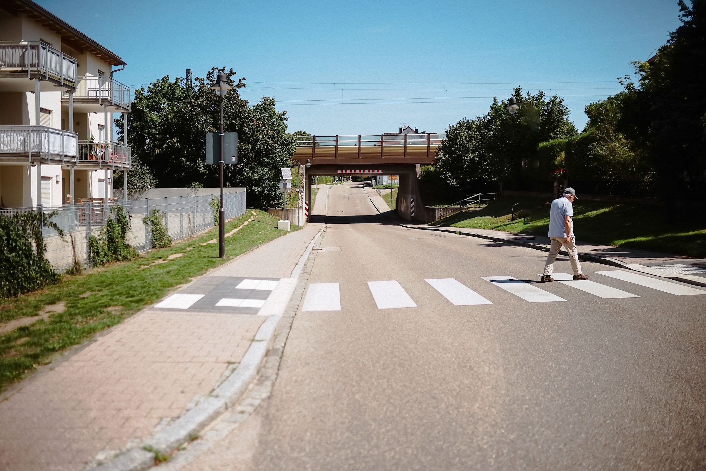 Ein älterer Mann überquert einen Zebrastreifen auf einer Straße unter einer Eisenbahnbrücke.