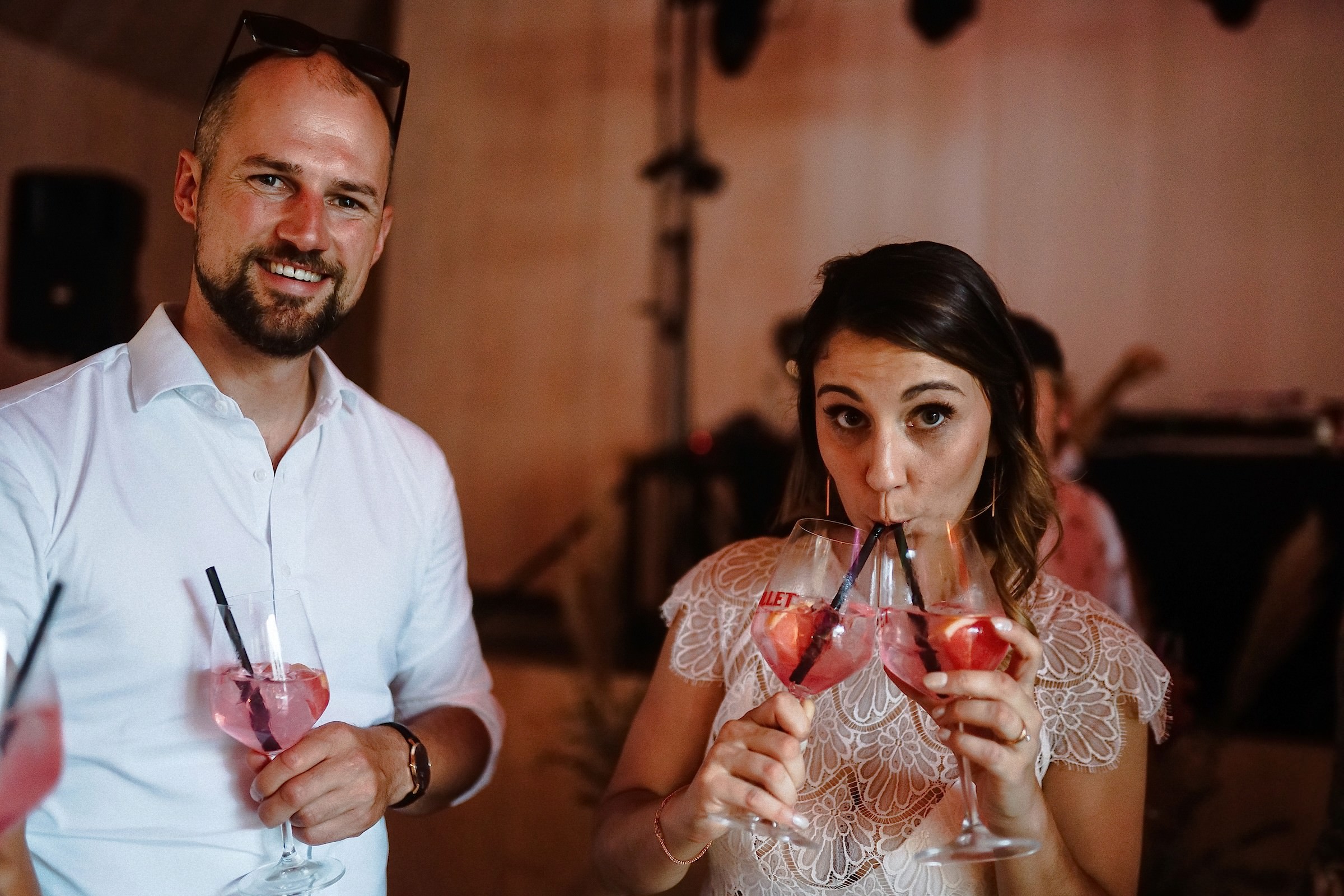 Ein Mann und eine Frau stoßen lachend mit rosa Cocktails an, die sie durch Strohhalme trinken.