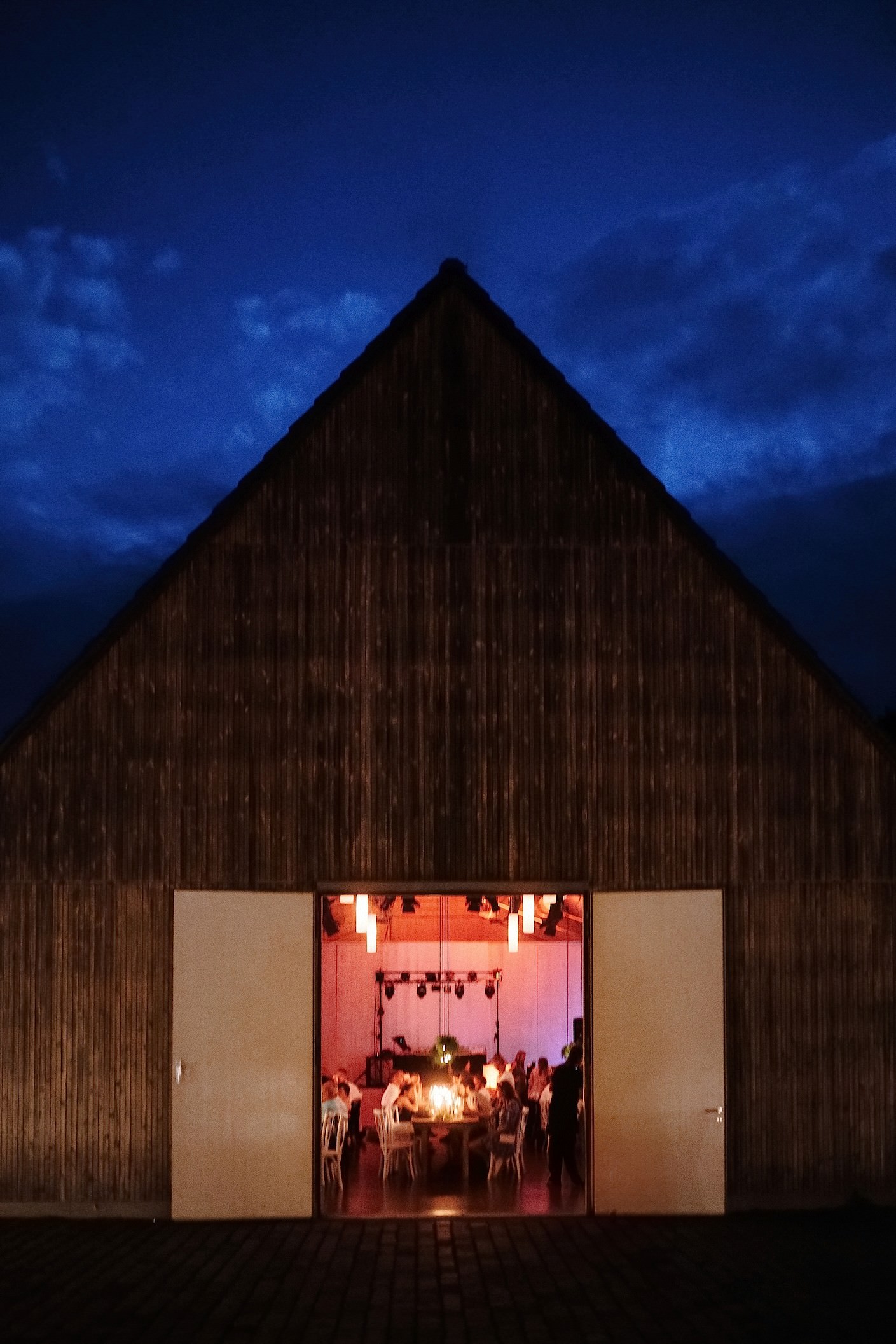 Die holzverkleidete Scheune leuchtet bei Abenddämmerung von innen, während drinnen die Gäste an der festlich gedeckten Tafel sitzen.