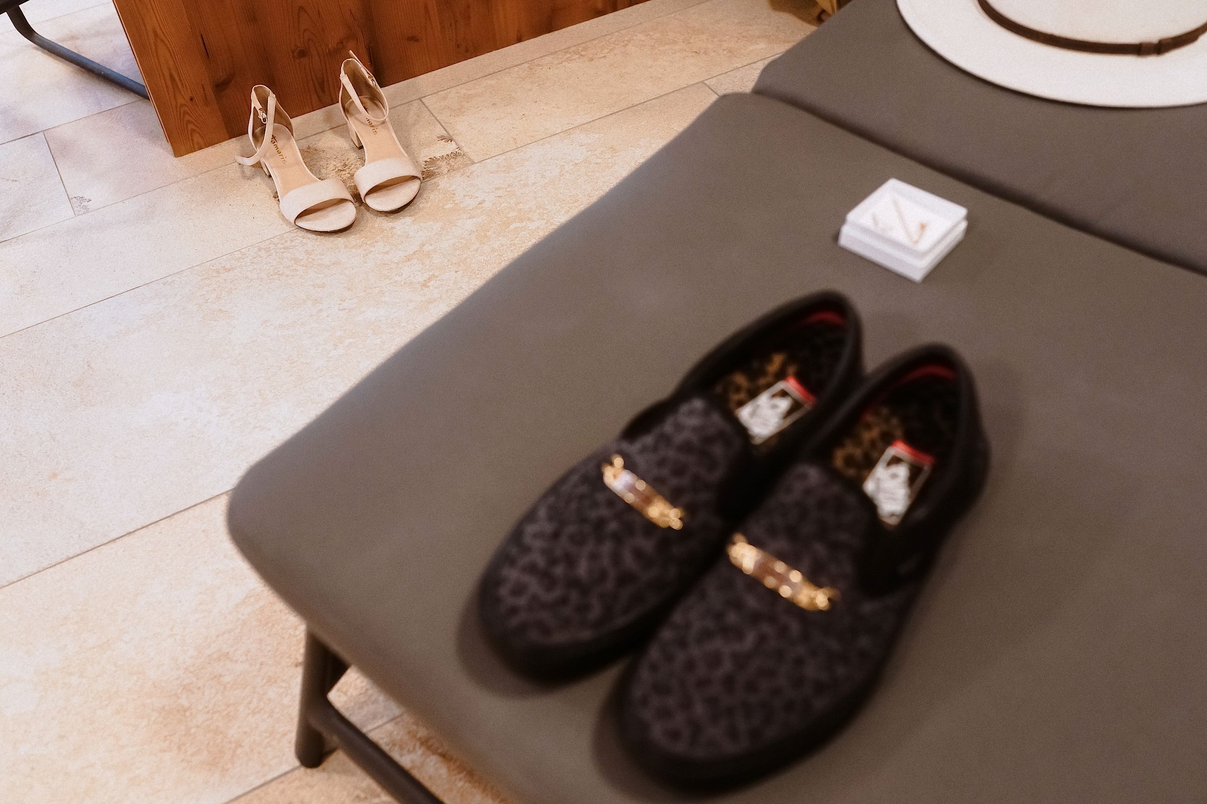 Die hellen Absatzschuhe der Braut stehen auf dem Boden, während die Leoparden-Slipper des Bräutigams samt Ringschachtel auf einer Bank bereitliegen.
