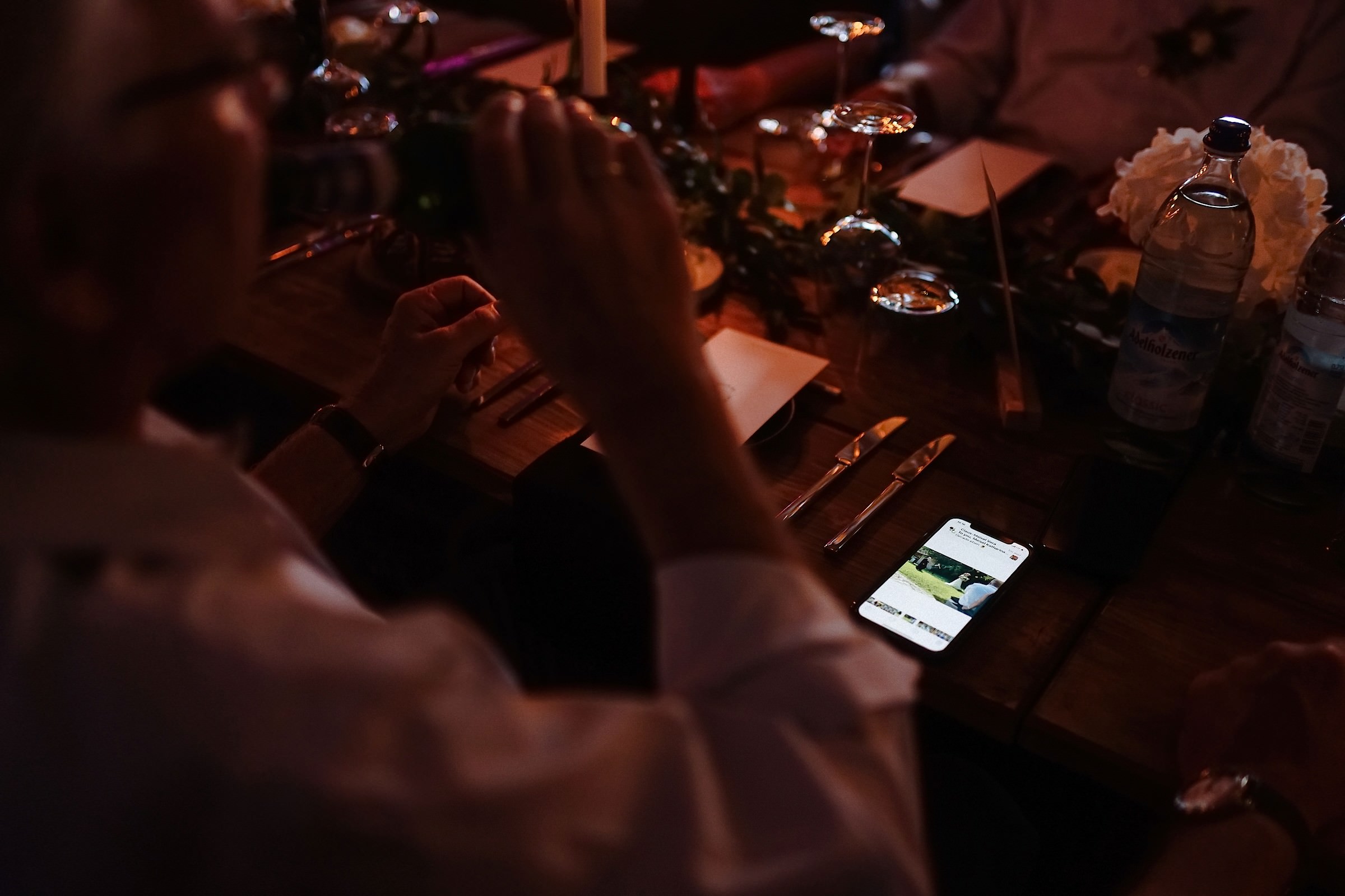 Im Kerzenlicht liegt ein leuchtendes Smartphone mit einem Hochzeitsfoto zwischen dem Besteck auf dem Tisch.
