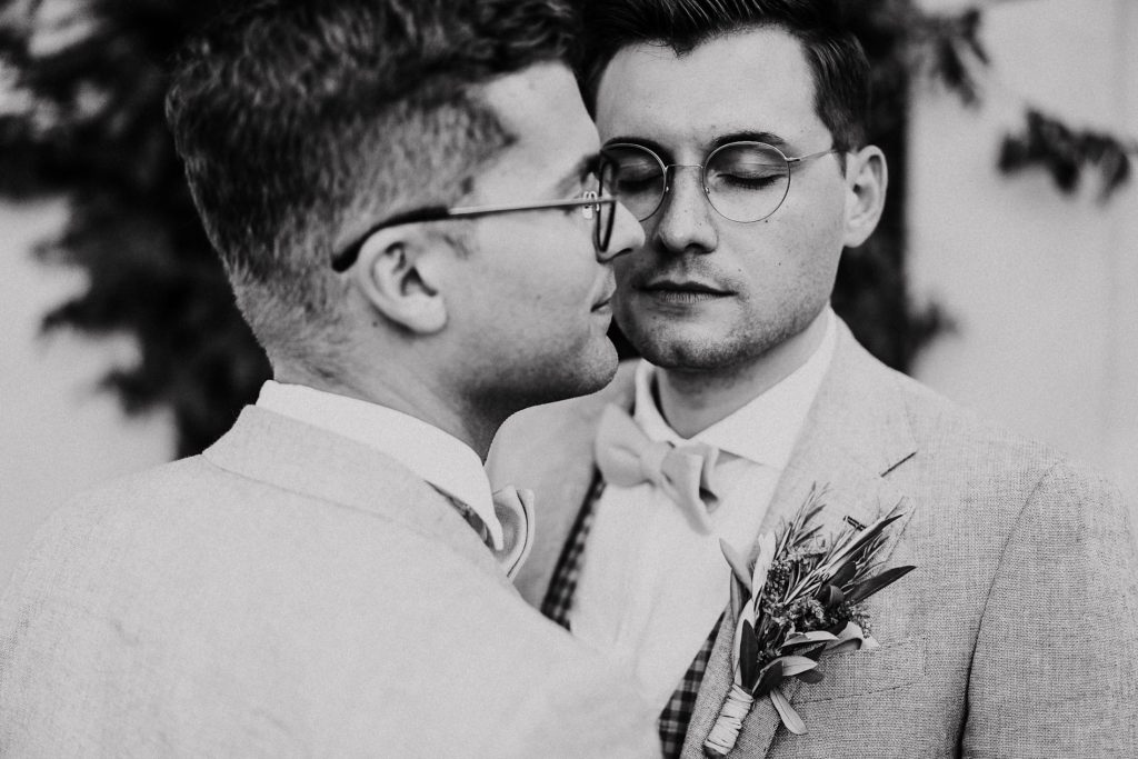 Zwei Bräutigame in Hochzeitsanzügen mit Boutonniere, Portrait mit geschlossenen Augen, schwarz-weiß.