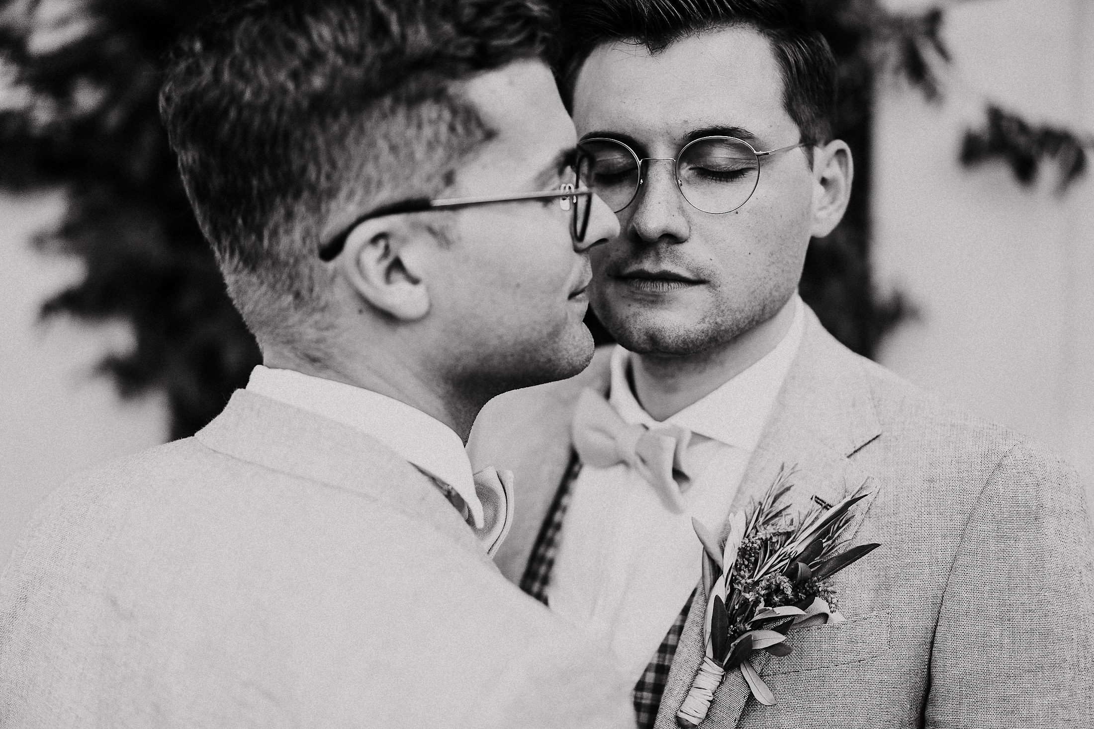Zwei Bräutigame in Hochzeitsanzügen mit Boutonniere, Portrait mit geschlossenen Augen, schwarz-weiß.