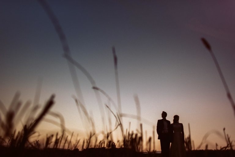 Die Silhouette des Brautpaares zeichnet sich im Sonnenuntergang mit Gräsern ab.