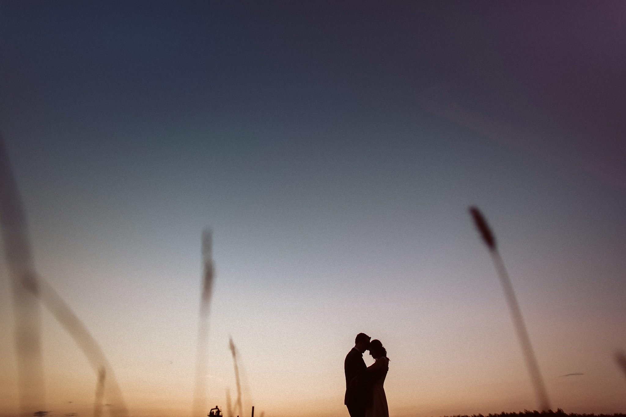 Das Brautpaar steht engagiert umschlungen in der Silhouette des Sonnenuntergangs.