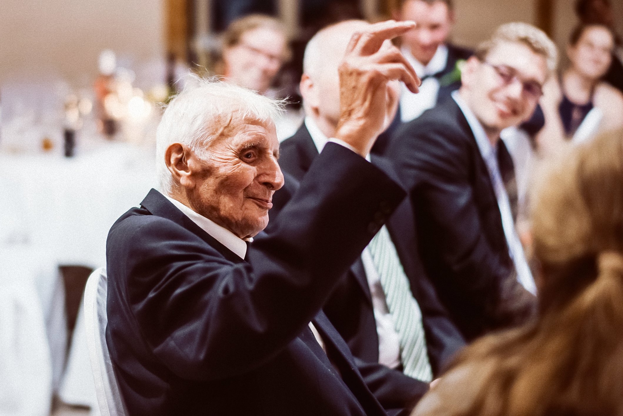 Älterer Herr winkt freudig auf Hochzeitsfeier, alle lachen zusammen.