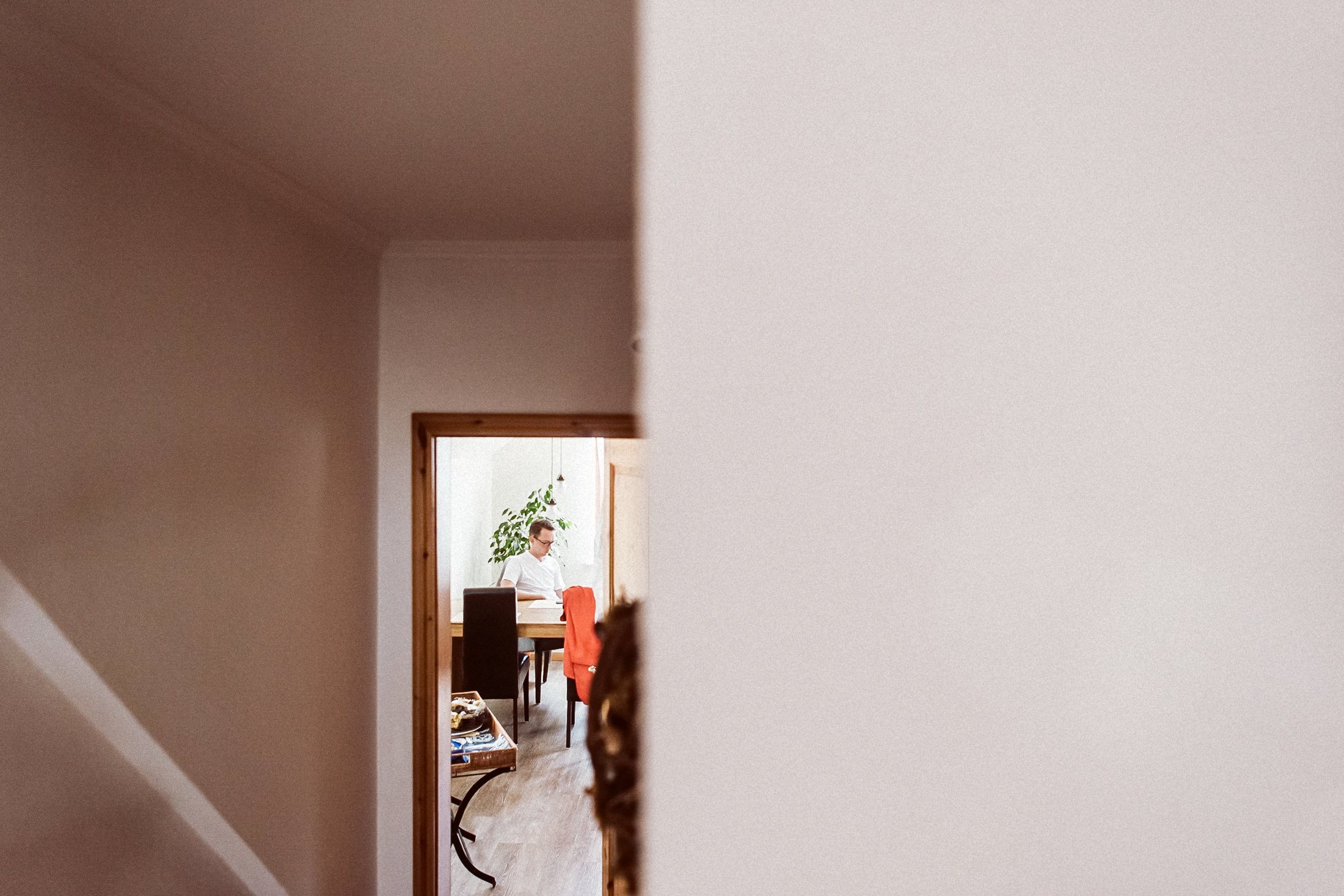 Bräutigam im Anzug sitzt wartend in Zimmer, durch offene helle Tür fotografiert.