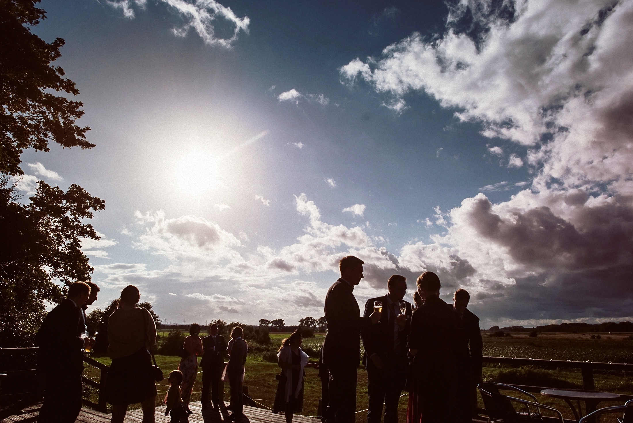 Hochzeitsgäste stehen auf Festterasse in Ostseebad Dahme gegen Sonne und Himmel.