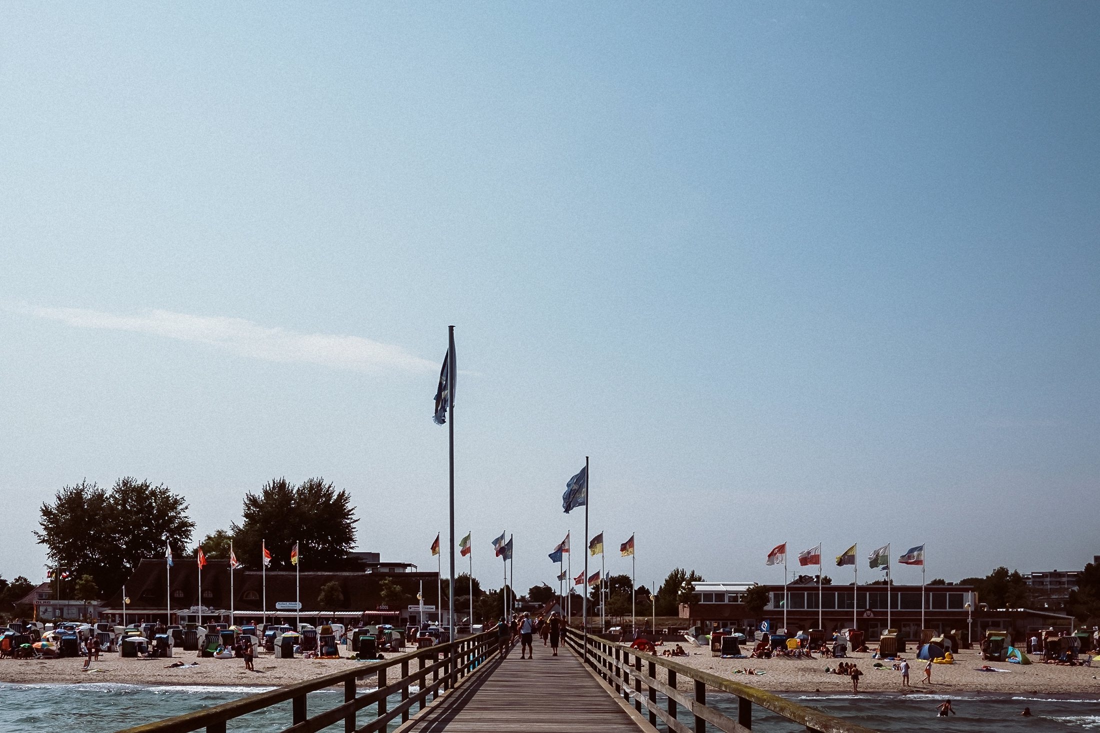 Holzsteg führt in Ostsee hinein, dahinter Strandkörbe und Besucherpavillon.