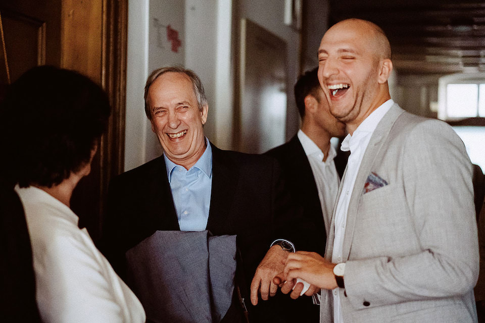 Bräutigam und ältere Männer lachen zusammen im golden beleuchteten Trausaal.