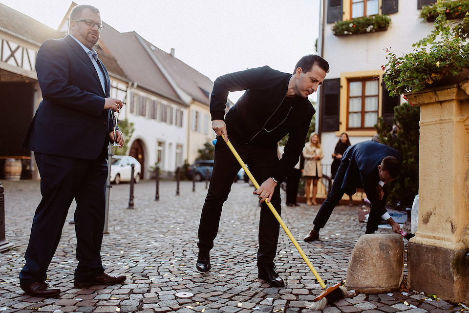 Gäste kehren Konfetti vom Platz vor Rathaus mit Besen weg.