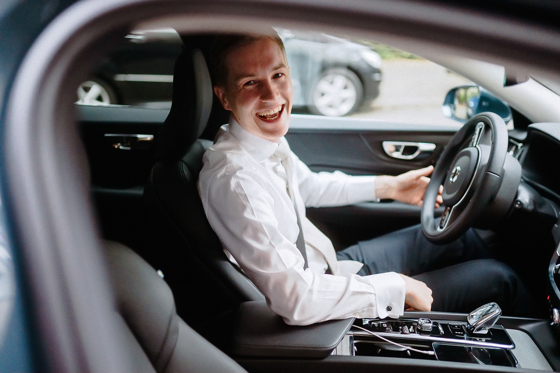 Der lachende Bräutigam sitzt am Steuer seines Autos vor der Fahrt zum Standesamt.