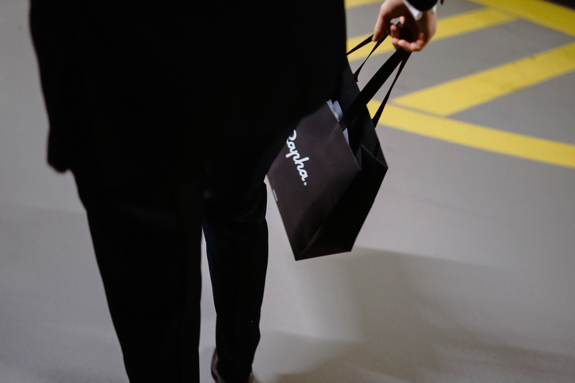 Ein Gast im Anzug trägt eine Rapha-Geschenktüte durch das Parkhaus.